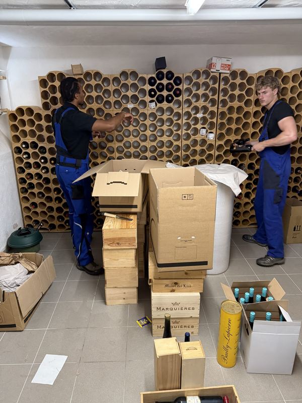 Weinkeller Flasche für Flasche einpacken Zwei Mitarbeiter räumen Weinflaschen aus dem Tonröhrenregal eines Kellers und verstauen sie in Holzkisten und Kartons